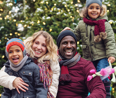 A couple and two children smile in front of a Christmas tree